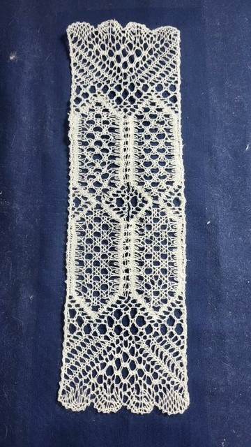 a long piece of lace made with bobbin lace in white on a dark blue background