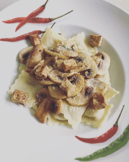 White plate with ravioli, mushrooms and baked tofu pieces.