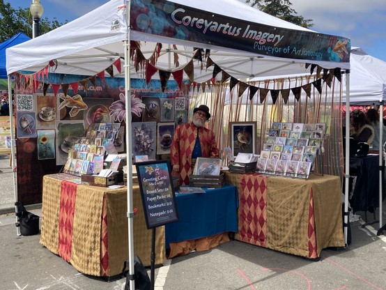 Photo of man in an art fair booth standing behind tables in a frock coat and bowler hat.