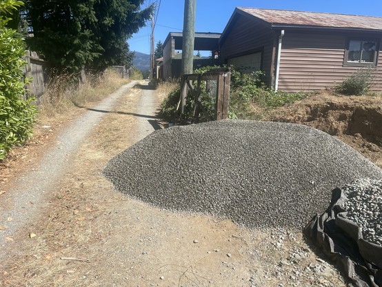 A large pile of grey pea gravel sits across the back yard fence line and nearly halfway into the alley