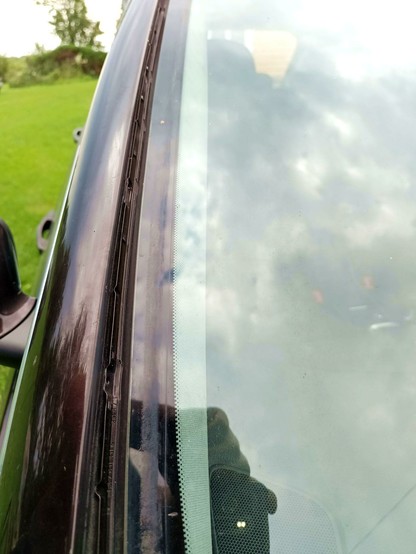 Passenger side of a car windshield with the trim removed, revealing some dirt and a metal rail for the trim to clip into, but no leak.
