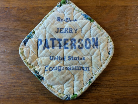 A small and well-used square potholder advises in blue text that the user "Re-elect Jerry Patterson, United States Congressman."