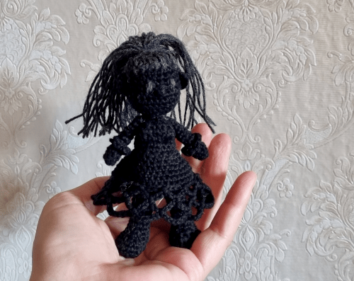 Nahaufnahme von einer gehäkelten Figur. Sie ist fast komplett aus schwarzer Wolle gemacht, nur die langen Haare und die Augen sind dunkelgrau.