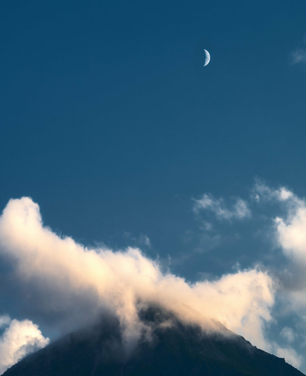 Halbmond am klaren Himmel über einem Berg, der von Wolken umgeben ist