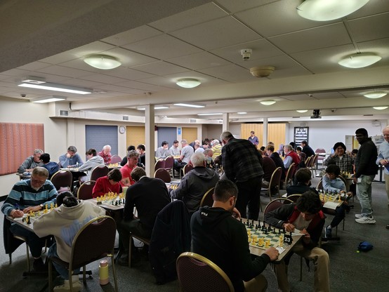 A low-ceilinged room full of players pondering their chess boards