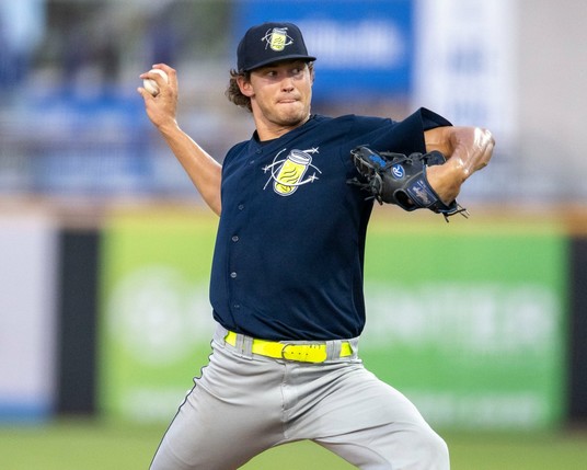 Josh Hansell winds up to throw a pitch while wearing a dark-colored uniform top and bright yellow belt.