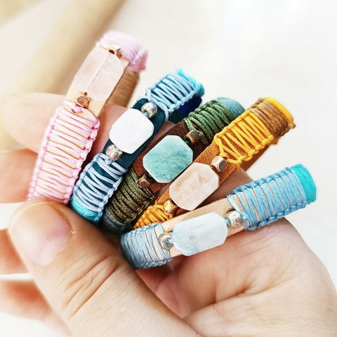 My hand holding 5 handmade leather bracelets of my "Luminous Elements" collection - simple women bracelets with a central semi-precious stone and macrame braiding - each one with its own personality, visual presence and energy properties.