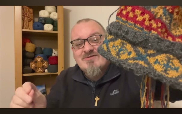 Andrew, a white dude,holding up a multi-colored knitted cap