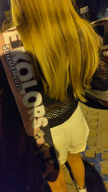 A blond girl from behind, a The Kolors scarf draped on her shoulder.