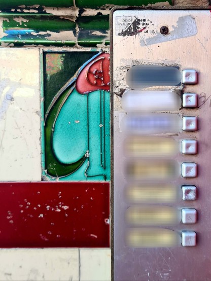 A decorative tenement tile half hidden by a modern intercom.
