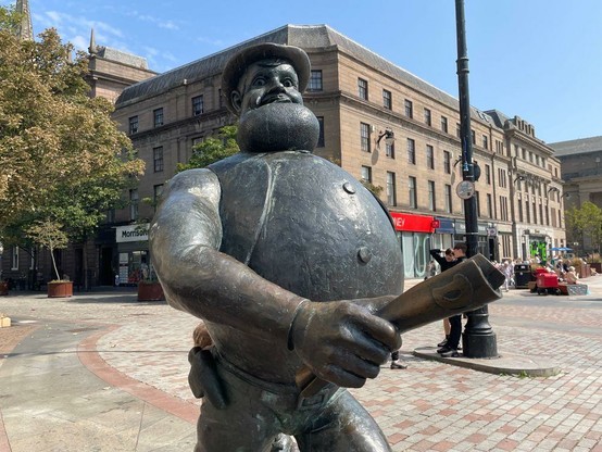 Bronze statue of Desperate Dan, a barrel chested man, striding.