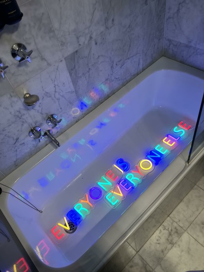 Neon lettering in a hotel bath which says everyone is everyone else