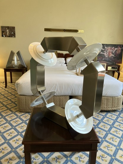 A sculpture made of dinner plates and metal bars in front of a hotel bed