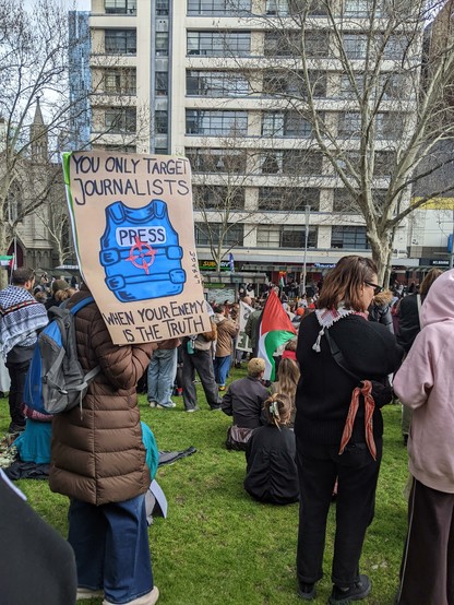 A photo of a free Palestine rally in Melbourne, Palestinian flags are in the background.
In the foreground there is a sign "you only target journalists when your enemy is the truth"