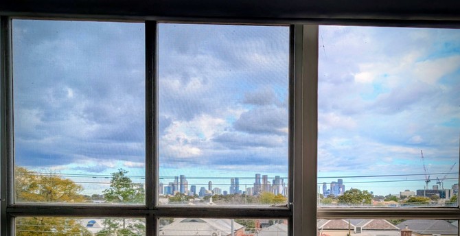 Through a 3-pane window. CBD skyline over rooftops. Ominous clouds above a strip of blue sky