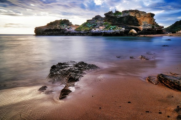 London Bridge at Portsea, on the Mornington Peninsula in Melbourne’s south, is a striking natural limestone arch sculpted by centuries of relentless wind and wave erosion. Once a full bridge connecting two sections of the cliff, part of the formation dramatically collapsed in 1990, leaving the rugged remnant that stands today as both a geological curiosity and a scenic landmark. Set against the wild surf of Bass Strait, the site is framed by golden sandstone cliffs, windswept dunes, and the untamed beauty of the surrounding coastline. Popular with walkers, photographers, and sightseers, London Bridge offers a window into the dynamic natural forces that continue to shape Victoria’s coastal landscape.