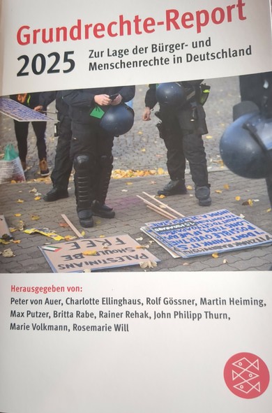 Buchcover mit Titel 'Grundrechte-Report 2025' und Untertitel 'Zur Lage der Bürger- und Menschenrechte in Deutschland'. Herausgeber: Peter von Auer, Charlotte Ellinghaus, Rolf Gössner, Martin Heiming, Max Putzer, Britta Rabe, Rainer Rehak, John Philipp Thurn, Marie Volkmann, Rosemarie Will.

Dazu ein Foto, das die Beine mehrerer uniformierter Polizisten zeigt. Vor diesen liegen Schilder einer Demonstration. Auf einem Schild ist zu lesen "Palestinians should be free"