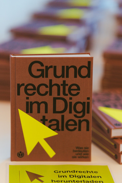Bild von einem braunen Buch mit dem TItel "Grundrechte im Digitalen" links ist ein Cursor zu sehen. Unten im Bild liegt ein grünes Schild auf dem steht: Grundrechte im Digitalen herunterladen.