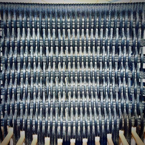 A blue woven pattern comprising the seat of a chair fills the frame from bottom to top.