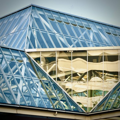 The glass-paned roof of a city building showcases five or more different angles and triangular shapes under a bright blue sky.