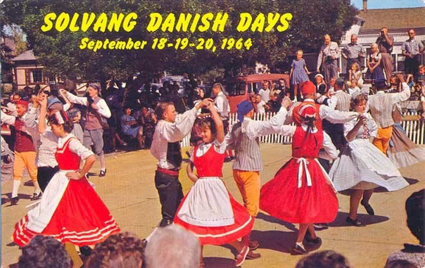 This postcard has a scene of people celebrating. In the center are five couples in traditional Danish costumes dancing. Above their heads across the green leaves of trees and yellow text says Solvang danish days September 18- 19th through 20th, 1964.