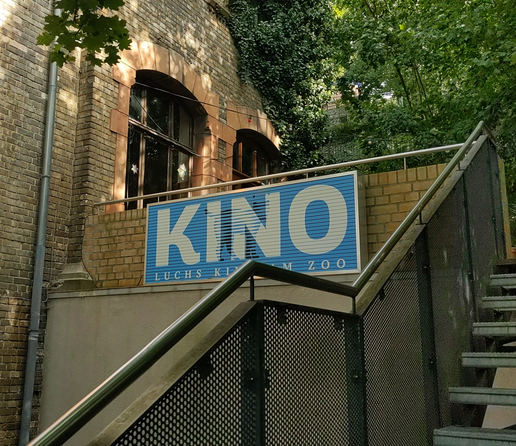 Schild mit dem Text „Kino“ in weiß auf hellblauem Grund an der Treppe zum Eingang des halleschen Luchs-Kinos.