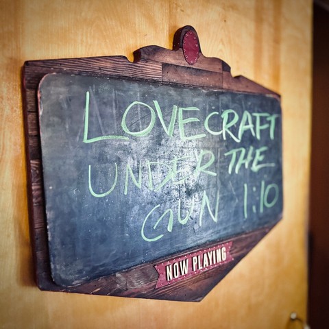 An interior movie screening door sign reads, "LOVECRAFT UNDER THE GUN 1:10 | NOW PLAYING."