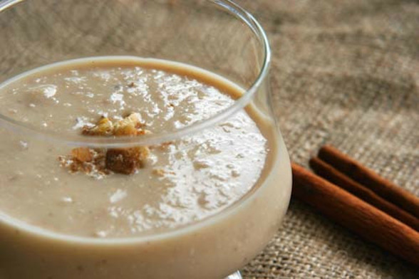 A glass bowl of cauliflower and walnut cream soup topped with some chopped walnuts. It sits on a woven cloth with a cinnamon stick in the background.
