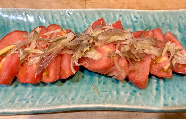 Tomato slices with sautéed myoga on top are presented on a light blue rectangular plate.