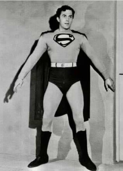 A black and white photo of actor Kirk Alyn in his Superman costume, with arms outstretched, and his cape down to only his knees.