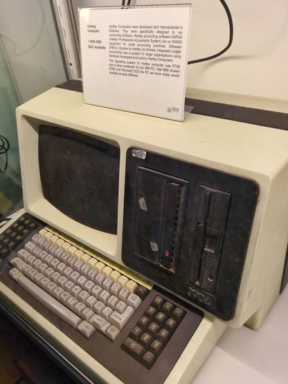 A long rectangular light beige computer with black disk drives and an embedded screen, with a two-tone grey keyboard.