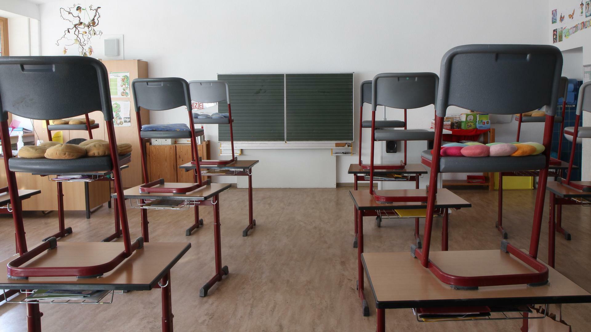 In einem leeren Klassenraum mit Tafel stehen die Stühle auf den Schultischen