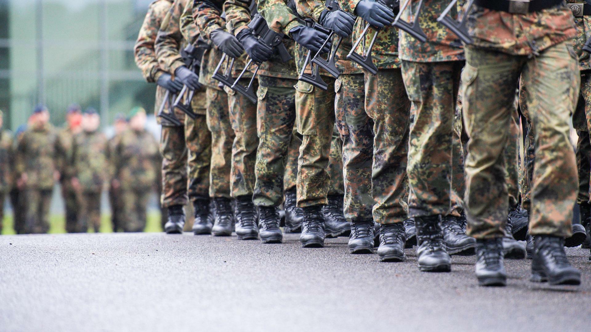 Soldaten marschieren mit Gewehr in Reih und Glied.