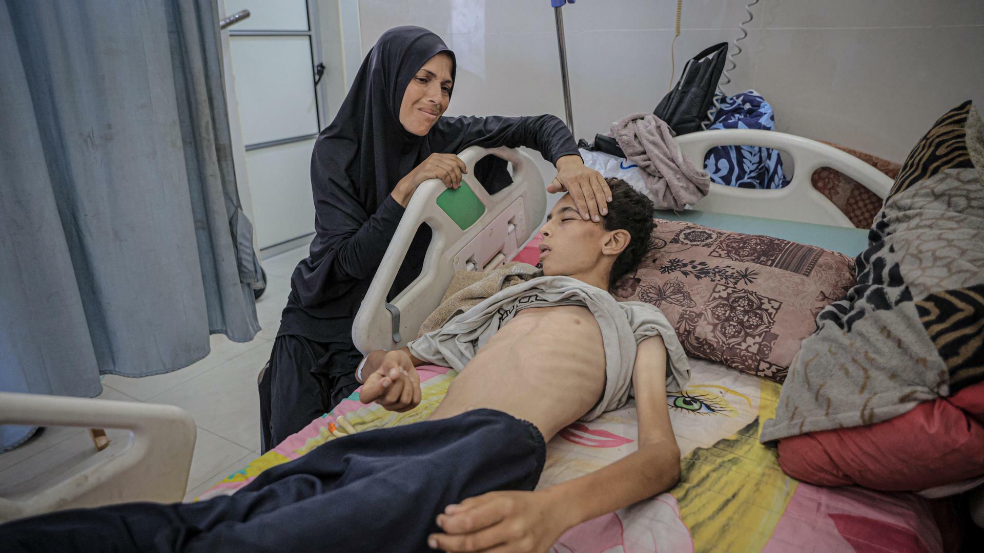 Ein stark abgemagerter Jugendlicher liegt im Al-Schifa-Krankenhaus in Gaza-Stadt in einem Krankenbett und wartet auf Behandlung. Seine Mutter kümmert sich um ihn.