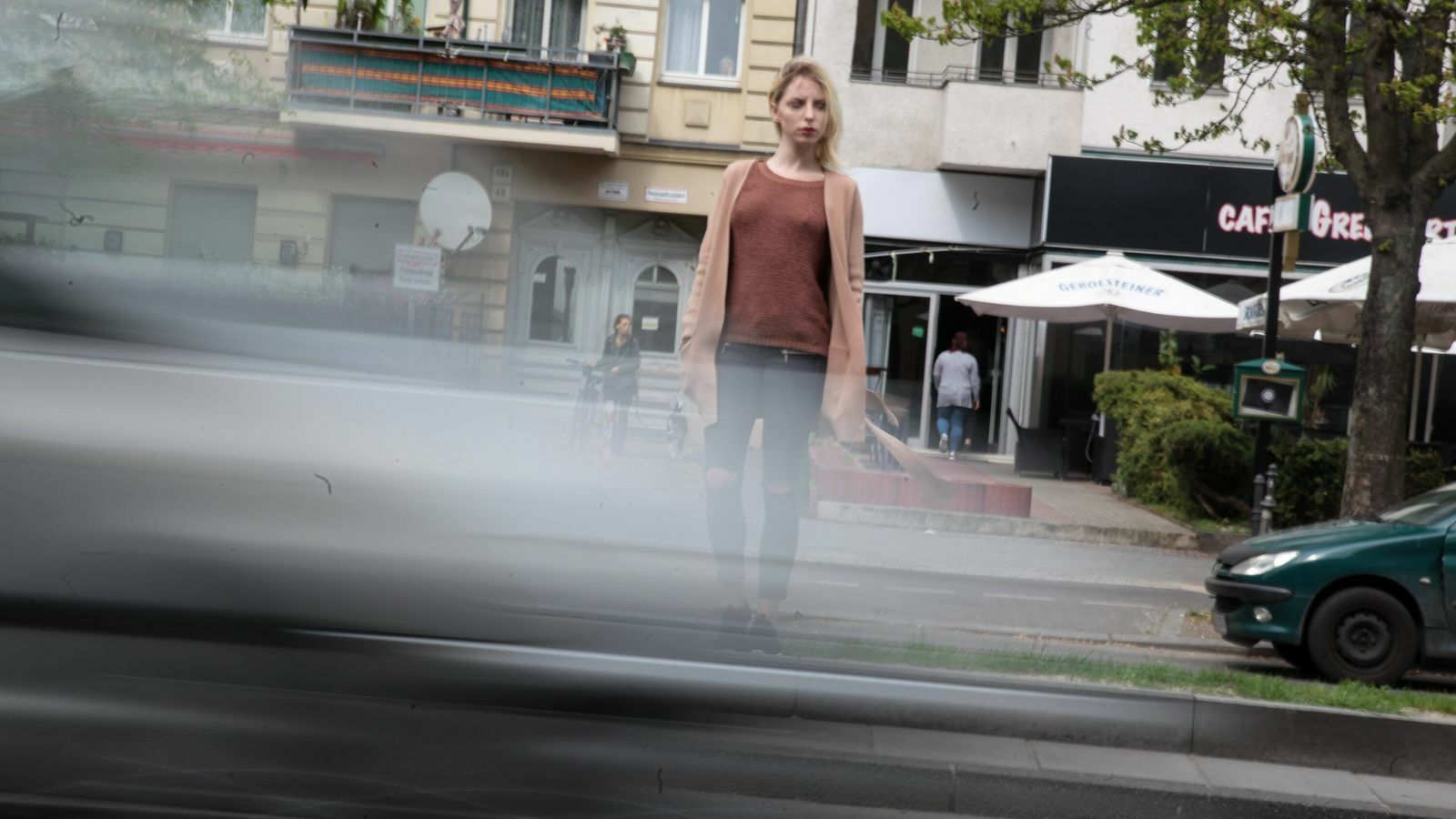 Junge Frau mit langen blonden Haaren steht am Straßenrand mit schnell an ihr vorbeifahrenden Autos