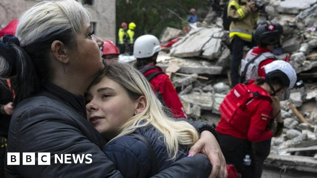 Two residents comfort each other as Ukrainian rescuers work among the rubble of a destroyed residential building following an air attack in Kyiv on 31 July 2025.