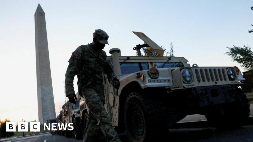 A soldier standing near the Washington Monument obelisk. He stands next to a military Humvee