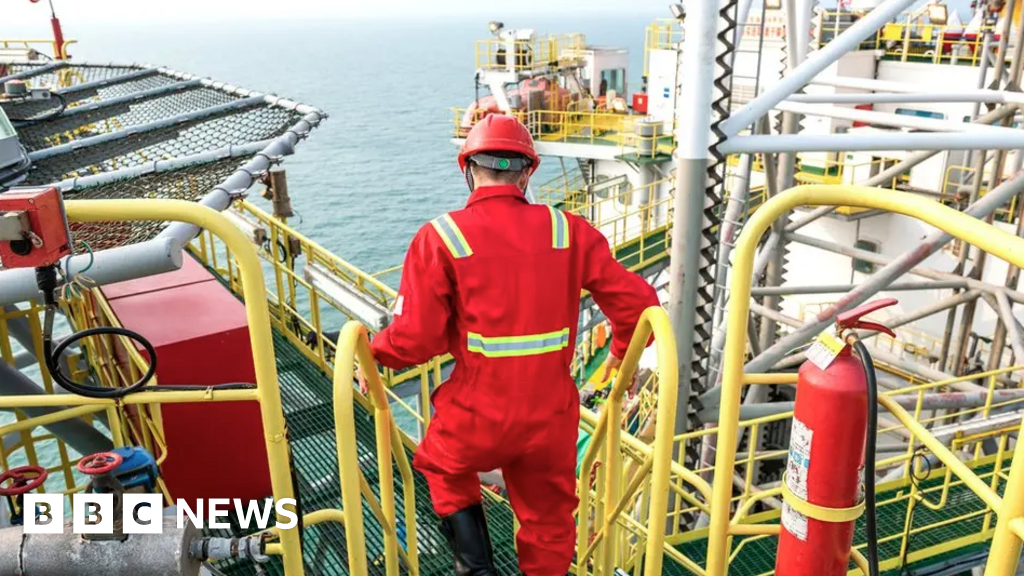 an oil worker in red overalls and safety hat descends steps on a North Sea rig