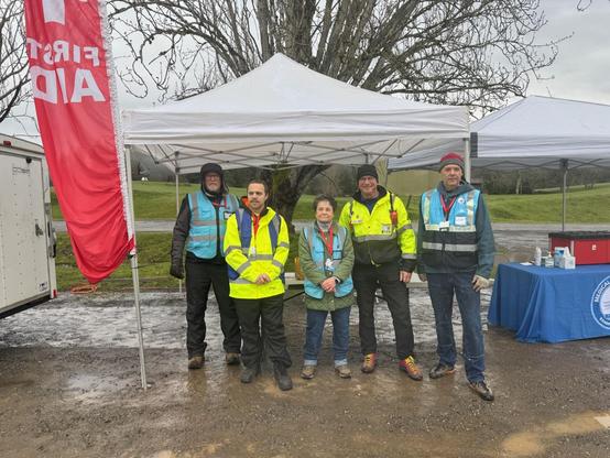 Me and four other volunteers wearing yellow and blue hi-vis gear standing in front of a tent with a "first aid" sign hanging up
