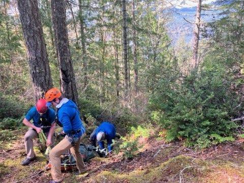 Several people in blue rain jackets and climbing helmets working with ropes to carry a rescue litter up a steep slope