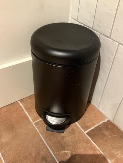 A black cylindrical trash can.