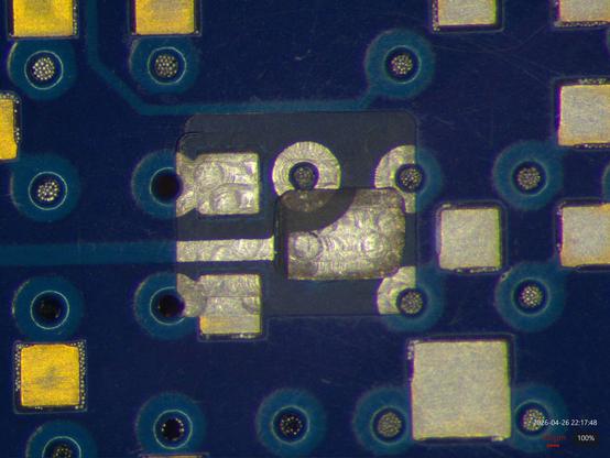 Microscope view of a two level cavity machined into a PCB with gold pads and blue soldermask. The first level stops at the top copper layer after removing soldermask, while a smaller inset goes down to layer 2 underneath. The top layer is well coated in shiny silver with some overspray to adjacent ENIG pads, while the smaller hole is bright and shiny in the middle but more dull along the edges of the hole that were harder to plate