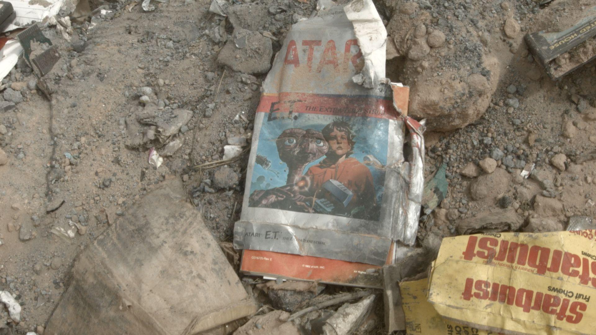 an Atari E.T. box crushed and covered in dirt next to a Starburst candy wrapper. for context, the E.T. game was so bad that Atari buried their excess copies in the New Mexico desert