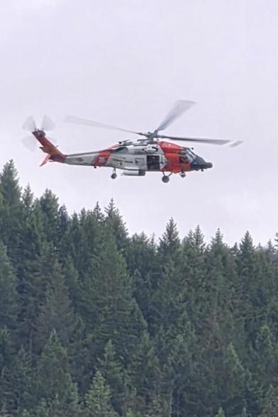US Coast Guard MH-60 helicopter hovering above a dense pine forest