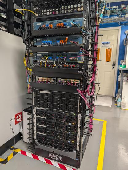 Front view of a server rack with five 2U servers, a 4U, two half width 1U QSFP28/QSFP+ switches, and three 1.5U 1G switches flanked by lots of decently neatly organized fiber and cat5 cables