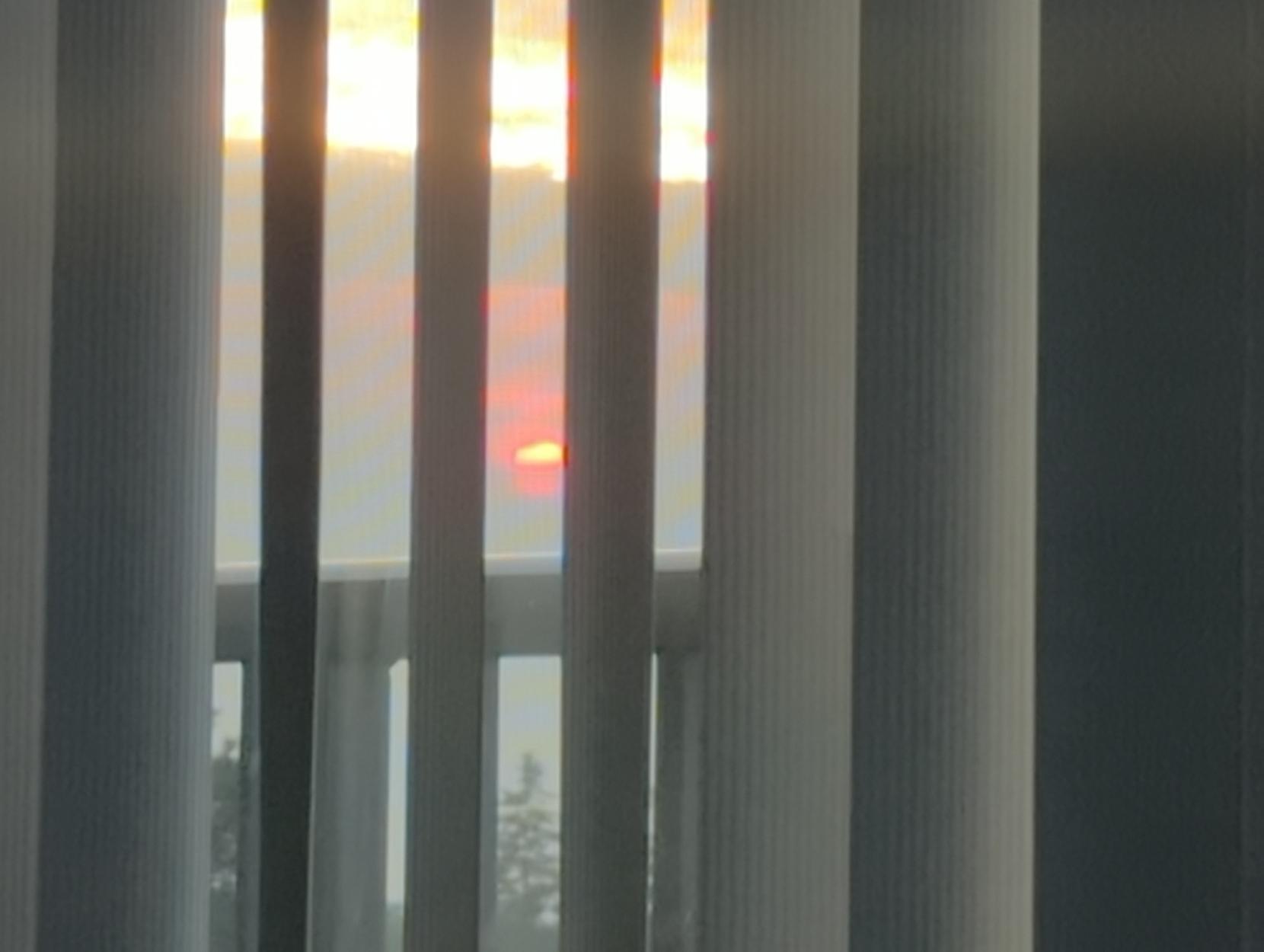 The red sun sets through the blinds