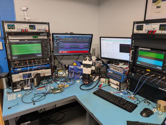 Lab bench with a green FPGA board cabled to many different pieces of test equipment