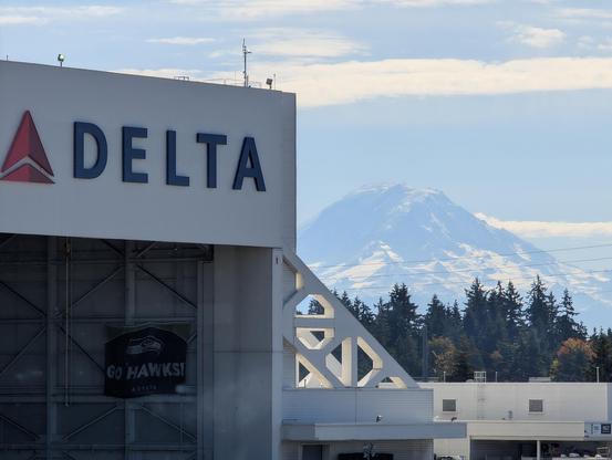 The snow capped top half of Mt. Rainier peeking out from the side of a Delta Airlines hangar on the south ramp at SEA