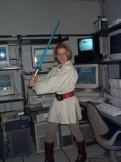 Woman dressed as a Star Wars Jedi Knight in a computer server room, holding a light saber. 