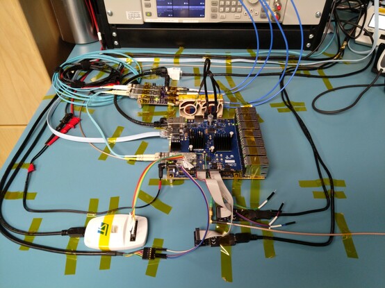 Test bench setup with gradually growing sea of cables around it including a cat5 Ethernet cable, a multimode fiber, a serial port, two fans, a barrel jack, two JTAG and one SWD adapters, and two power rail probe cables on test points